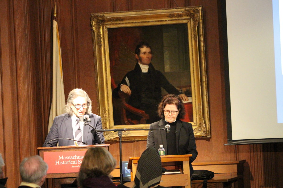 Man and Woman standing at podiums speaking to a seated audience